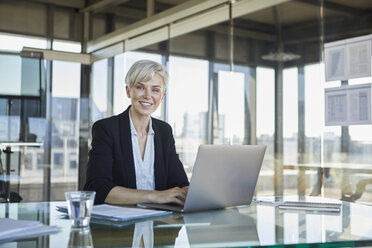 Porträt einer selbstbewussten Geschäftsfrau, die mit einem Laptop am Schreibtisch sitzt - RBF06916