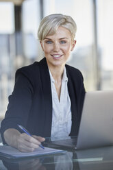 Portrait of confident businesswoman sitting at desk in office with laptop - RBF06918