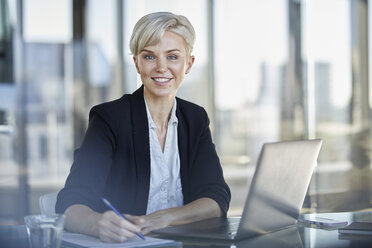 Portrait of confident businesswoman sitting at desk in office with laptop - RBF06919