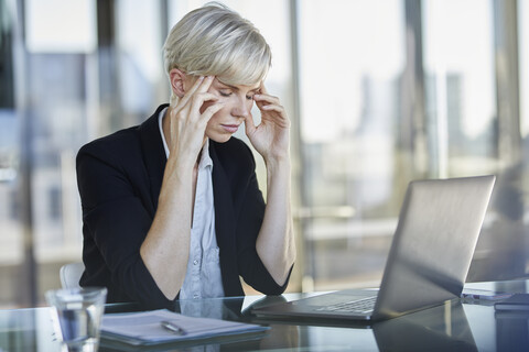 Exhausted businesswoman sitting at desk in office with closed eyes stock photo