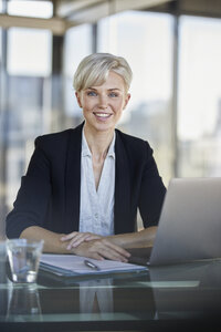Porträt einer lächelnden Geschäftsfrau am Schreibtisch im Büro mit Laptop - RBF06923