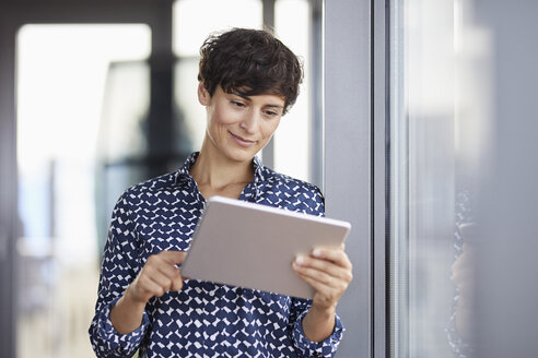 Lächelnde Geschäftsfrau mit Tablet am Fenster im Büro - RBF06931