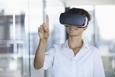 Businesswoman wearing VR glasses in office raising her finger - RBF06939