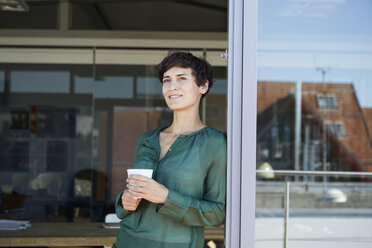 Smiling woman standing at the window having a coffee break - RBF06941
