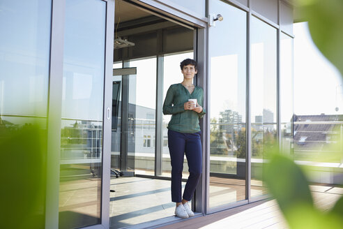 Lächelnde Frau, die am Fenster steht und eine Kaffeepause macht - RBF06943