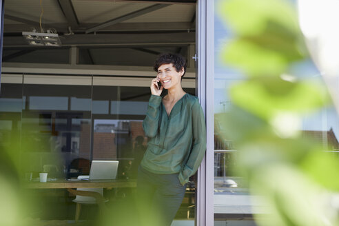 Smiling woman standing at the window talking on cell phone - RBF06944