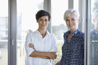 Portrait of two smiling businesswomen at the window in office - RBF06951