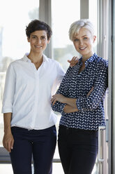 Portrait of two smiling businesswomen at the window in office - RBF06952