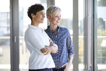 Zwei lächelnde Geschäftsfrauen schauen im Büro aus dem Fenster - RBF06954