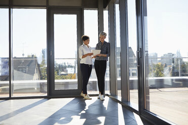 Two businesswomen discussing document at the window in bright office - RBF06956