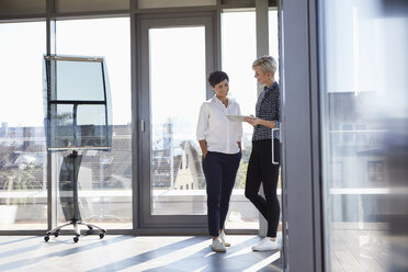 Two smiling businesswomen looking at tablet at the window in bright office - RBF06957