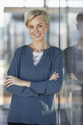 Portrait of smiling woman leaning against window - RBF06972
