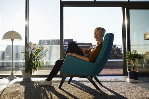 Portrait of smiling woman sitting in armchair in sunlight - RBF06975