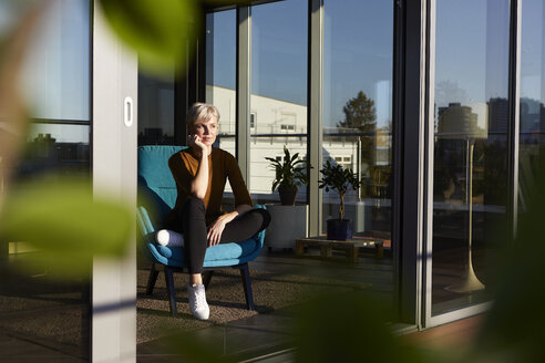 Woman sitting in armchair looking out of window - RBF06978