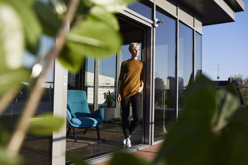 Frau steht am Fenster auf der Dachterrasse - RBF06979