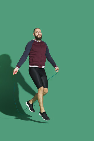 Porträt eines bärtigen Mannes, der vor einem grünen Hintergrund Seil springt, lizenzfreies Stockfoto