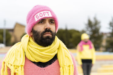 Porträt eines bärtigen Schwulen mit Nasenpiercing, der eine rosafarbene Kappe mit dem Wort 