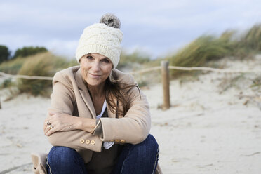 Spain, Menorca, portrait of smiling senior woman wearing bobble hat on the beach in winter - IGGF00696