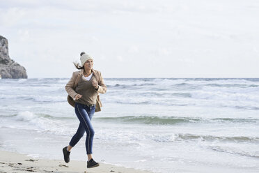 Spanien, Menorca, ältere Frau beim Joggen am Strand im Winter - IGGF00697