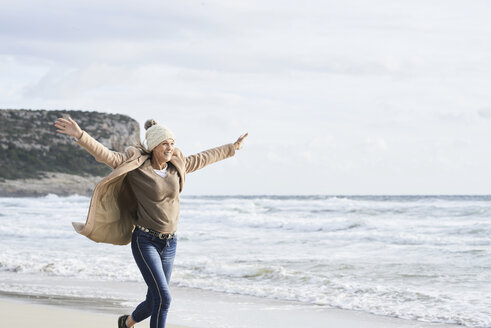 Spain, Menorca, happy senior woman running on the beach in winter - IGGF00699