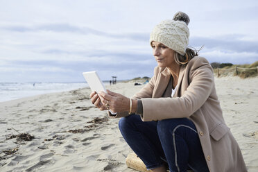 Spain, Menorca, senior woman reading E-Book on the beach in winter - IGGF00701