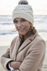 Spain, Menorca, portrait of smiling senior woman wearing bobble hat on the beach in winter - IGGF00706