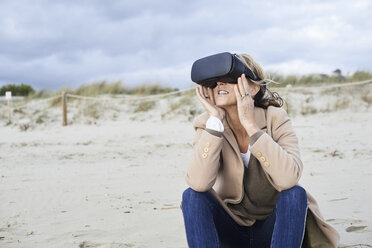 Spanien, Menorca, ältere Frau mit VR-Brille am Strand im Winter - IGGF00712