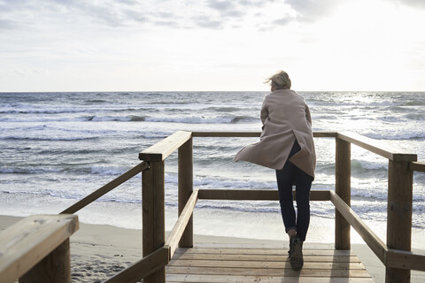 Spanien, Menorca, Rückenansicht einer älteren Frau, die im Winter auf der Strandpromenade steht und auf das Meer schaut, lizenzfreies Stockfoto