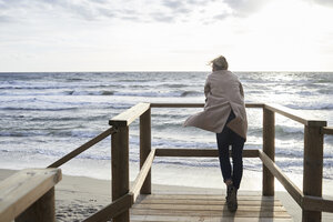 Spanien, Menorca, Rückenansicht einer älteren Frau, die im Winter auf der Strandpromenade steht und auf das Meer schaut - IGGF00715