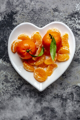 Mandarinen mit Blättern, Stücke auf herzförmigem Teller, lizenzfreies Stockfoto
