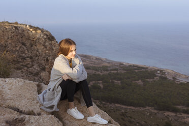 Spain, Alicante, Santa Pola, Cape Santa Pola, young woman sitting on rock at sunset - GRSF00037