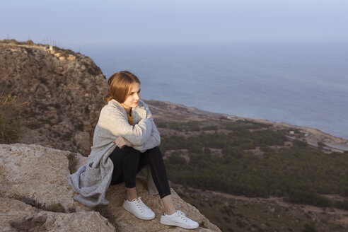 Spanien, Alicante, Santa Pola, Kap Santa Pola, junge Frau sitzt bei Sonnenuntergang auf einem Felsen - GRSF00037