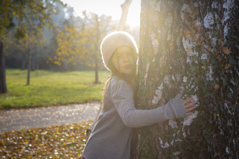 Junges Mädchen umarmt Baum im Herbst, lizenzfreies Stockfoto