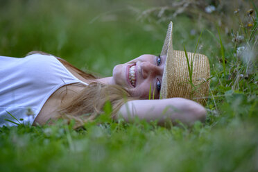Portrait of laughing teenage girl wearing straw hat lying on a meadow in summer - LBF02315
