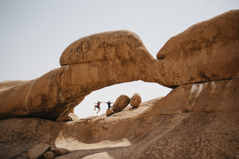 Namibia, Spitzkoppe, zwei Freunde springen auf eine Felsformation - LHPF00347