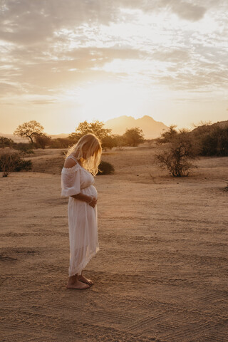 Namibia, Spitzkoppe, Frau im weißen Kleid in Wüstenlandschaft bei Sonnenuntergang, lizenzfreies Stockfoto