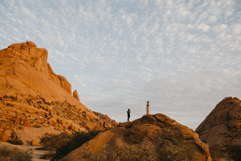 Namibia, Spitzkoppe, Paar bei Sonnenuntergang auf einem Felsen stehend - LHPF00368