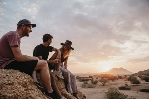 Namibia, Spitzkoppe, Freunde sitzen bei Sonnenuntergang auf einem Felsen, lizenzfreies Stockfoto