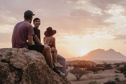 Namibia, Spitzkoppe, Freunde sitzen bei Sonnenuntergang auf einem Felsen - LHPF00379