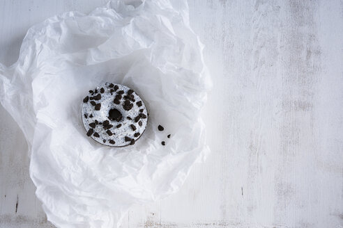 Krapfen mit weißem Zuckerguss und dunklen Schokoladensplittern auf weißem Seidenpapier - OJF00318