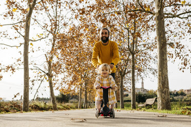 Vater und Tochter genießen einen morgendlichen Tag im Park im Herbst, Mädchen auf Motorroller - JRFF02253
