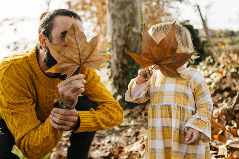 Father and daughter enjoying a morning day in the park in autumn, playing with autumn leaves - JRFF02254