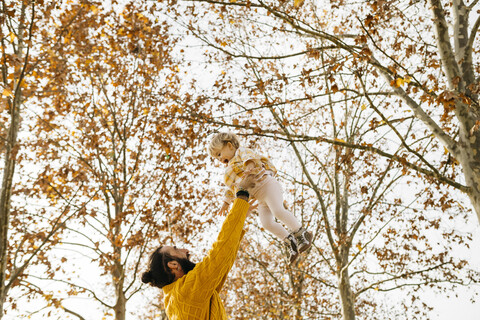 Vater wirft seine Tochter in die Luft, in einem Park im Herbst, lizenzfreies Stockfoto