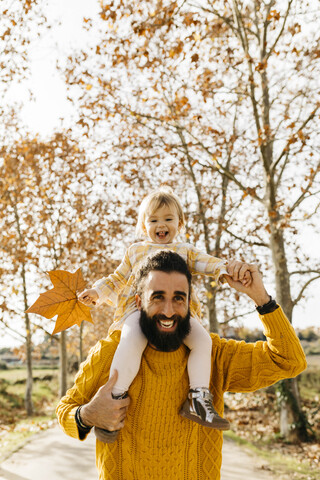 Vater trägt seine kleine Tochter auf den Schultern am Morgen in einem Park im Herbst, lizenzfreies Stockfoto