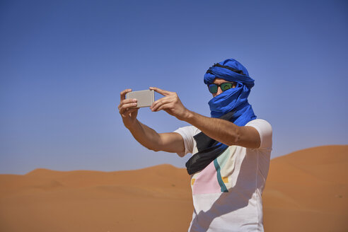 Marokko, Mann mit Sonnenbrille und blauem Tuban fotografiert mit Smartphone in der Wüste - EPF00515