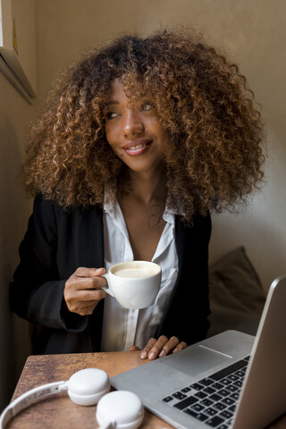 Junge Frau mit Laptop in einem Café, die einen Kaffee trinkt, lizenzfreies Stockfoto