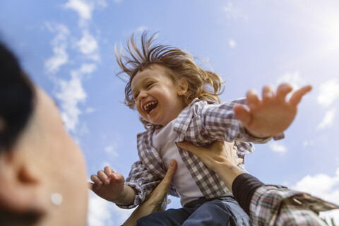 Mutter hebt glückliches Kleinkind im Freien hoch, lizenzfreies Stockfoto