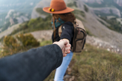 Frau mit Hut, auf einem Berg stehend, hält sich an der Hand eines Mannes fest, lizenzfreies Stockfoto