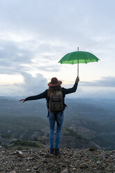Frau auf einem Berg stehend, mit Blick auf die Aussicht, hält einen grünen Regenschirm - AFVF02205