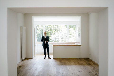 Ein Immobilienmakler wartet mit einem Laptop in seinem neu renovierten Haus, lizenzfreies Stockfoto